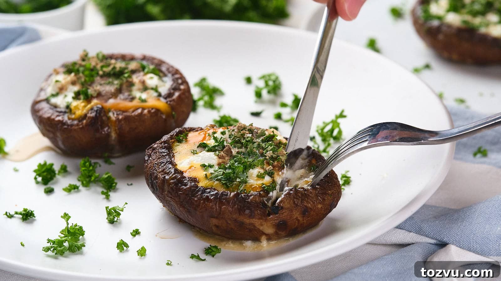 17 Thanksgiving Recipes Ready in Minutes 18 A fork and knife cutting into an egg in mushroom with green garnish visible in the background.