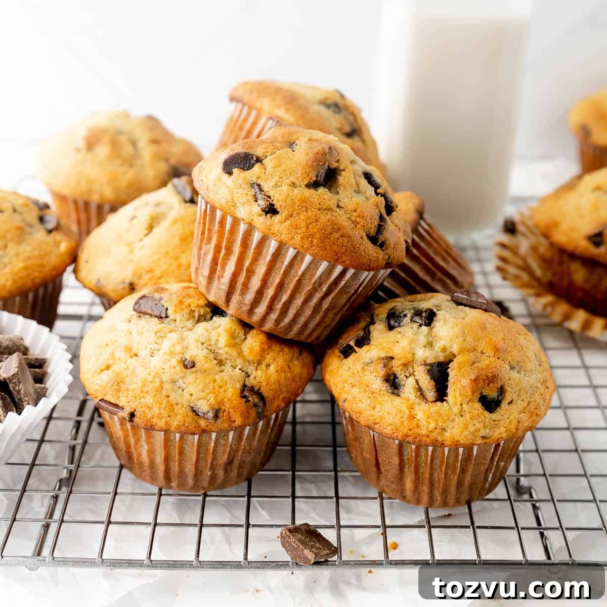 A pile of banana muffins with chocolate chunks on a cooling rack.
