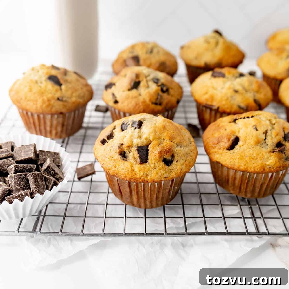 Muffins on a cooling rack. Chocolate chunks on the side and a bottle of milk in the back.