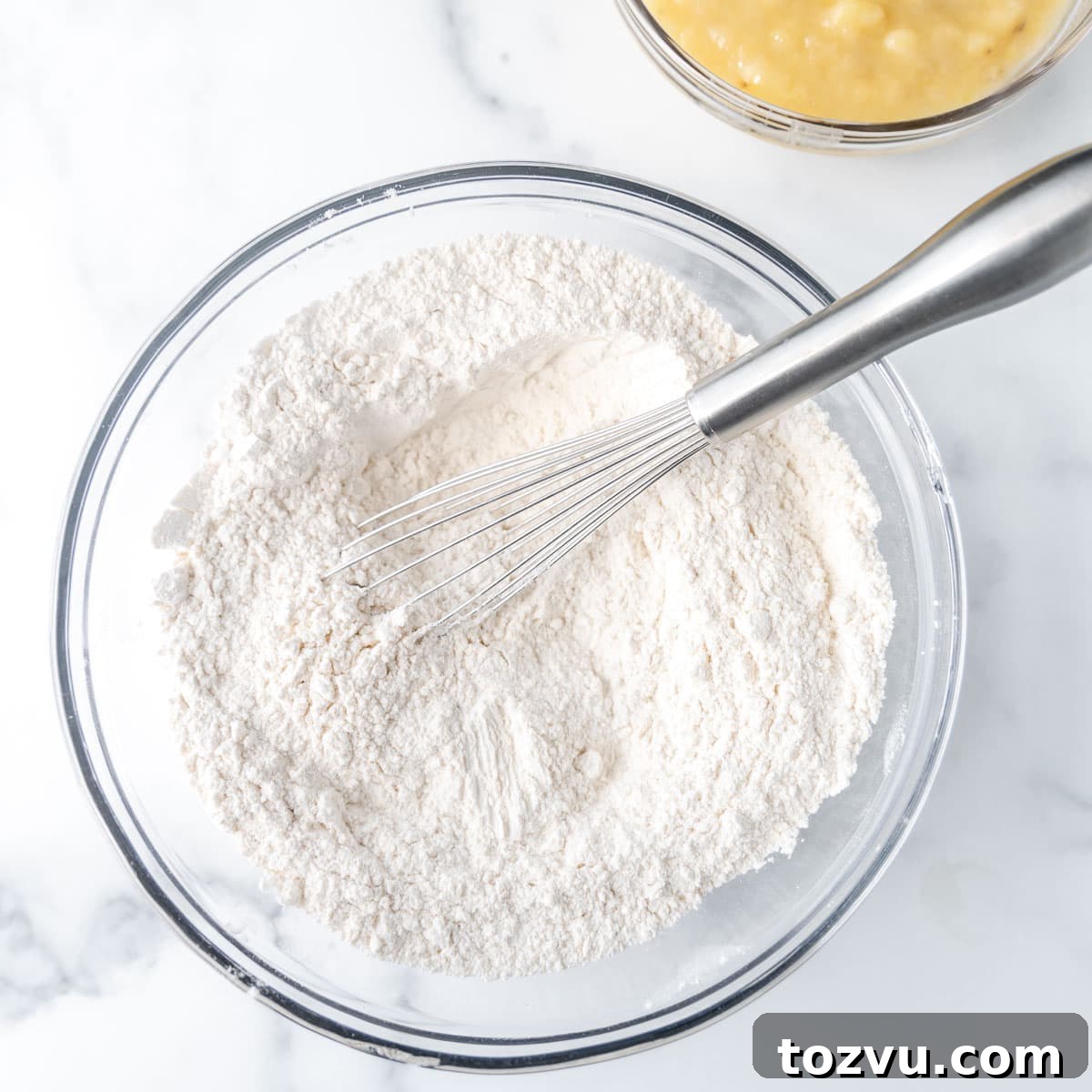 Dry ingredients in a clear bowl with a whisk.