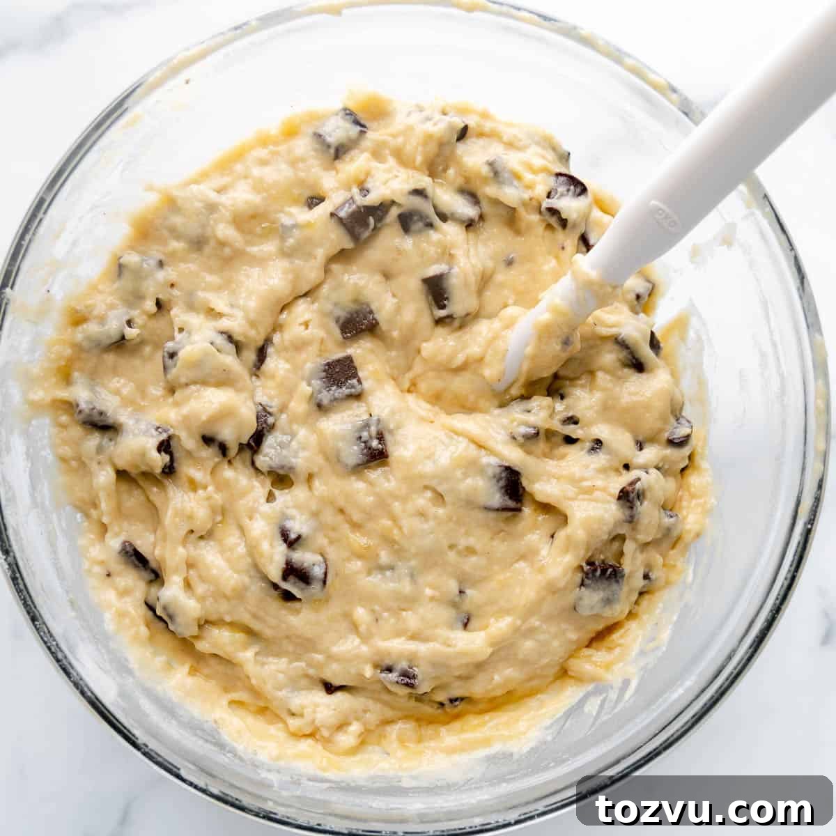 Muffin batter in a mixing bowl with a white spatula.